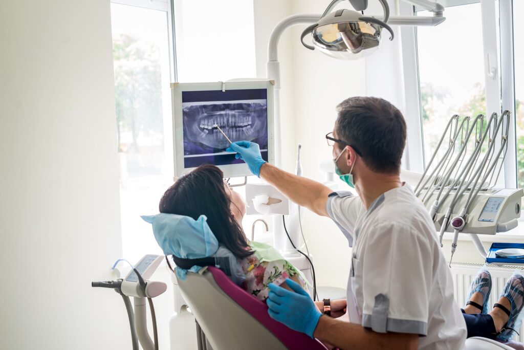 image of a woman sitting in a dental chair with the dentist pointing at at digital xray of her teeth